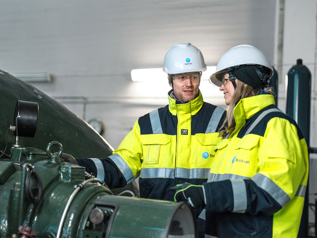 Inside Svean hydro power plant where two Statkraft colleagues stand next to a power turbine.